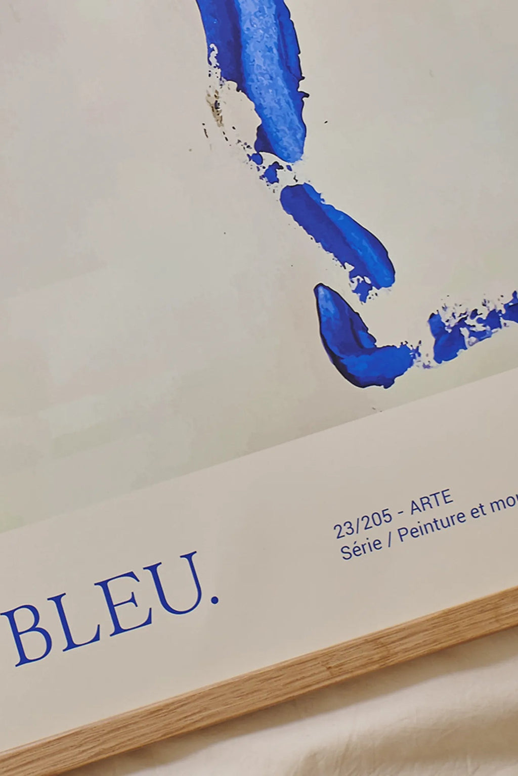 The Poster Club Bleu, a vibrant modern abstract art print featuring bold royal blue brushstrokes with a painted texture on a clean off-white background, titled 'BLEU.' in dark blue serif font. This minimalist poster is elegantly presented in a light natural oak frame, ideal for contemporary gallery walls, Scandinavian living rooms, or creative home office decor.
