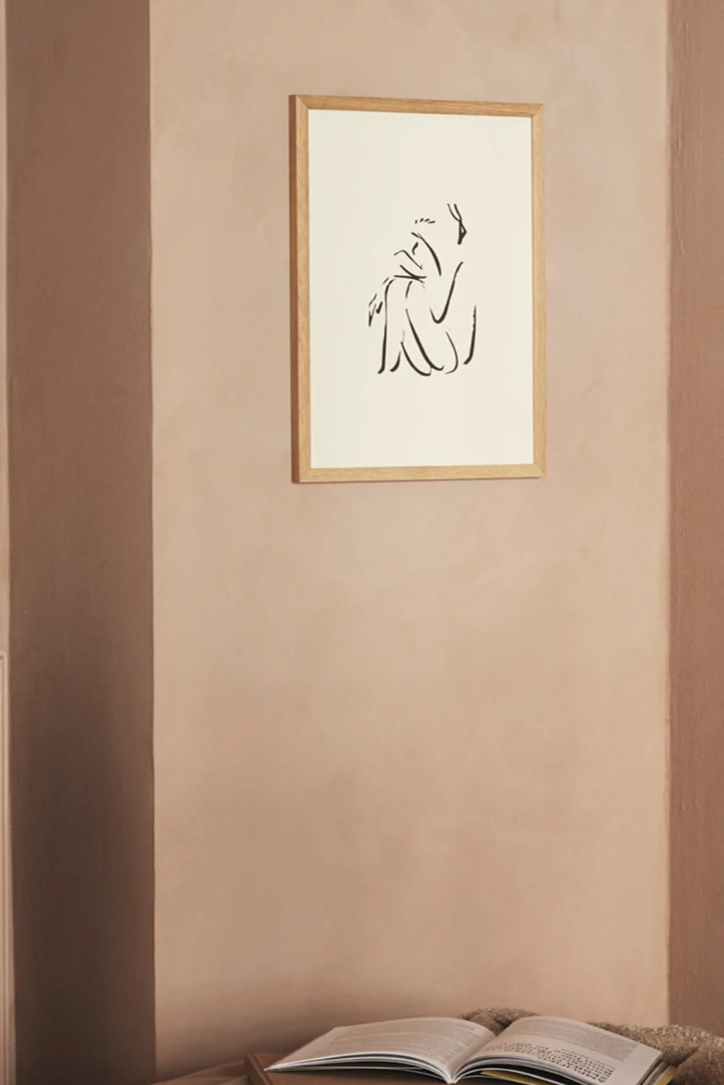The Poster Club Calm, a minimalist abstract line art print featuring a fluid black silhouette of a sitting figure on a warm off-white background, elegantly framed in a light natural oak wood frame. Perfect for creating a serene focal point in Scandinavian living rooms, organic modern bedrooms, or contemporary gallery walls.