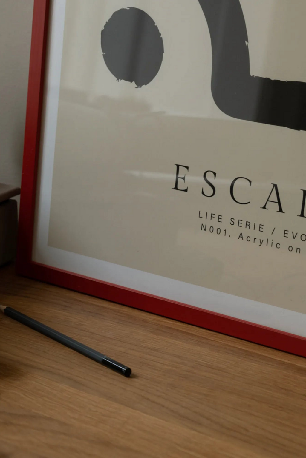 The Poster Club Escalar, a minimalist abstract art print featuring bold dark grey organic shapes, including a circle and a curved line, against a warm cream-colored background, professionally framed in a vibrant red wooden frame with a crisp white mat. This contemporary wall art is ideal for creating a focal point in modern living rooms or enriching a gallery wall with graphic design.