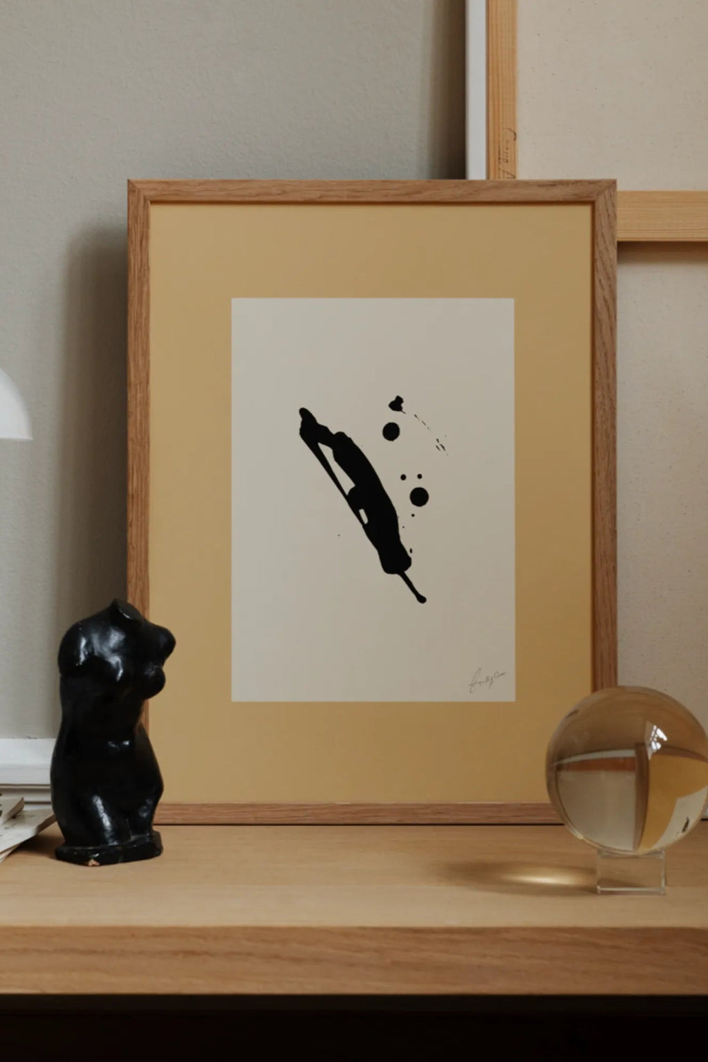The Poster Club Imagine, an abstract black ink art print featuring organic blotches and splatters on off-white paper, framed in a natural light oak frame with a striking mustard yellow passepartout. This minimalist artwork offers a bold yet subtle contemporary aesthetic with its fluid black shapes. Ideal for modern living rooms, Japandi bedrooms, or creative shelf styling in design-forward interiors.