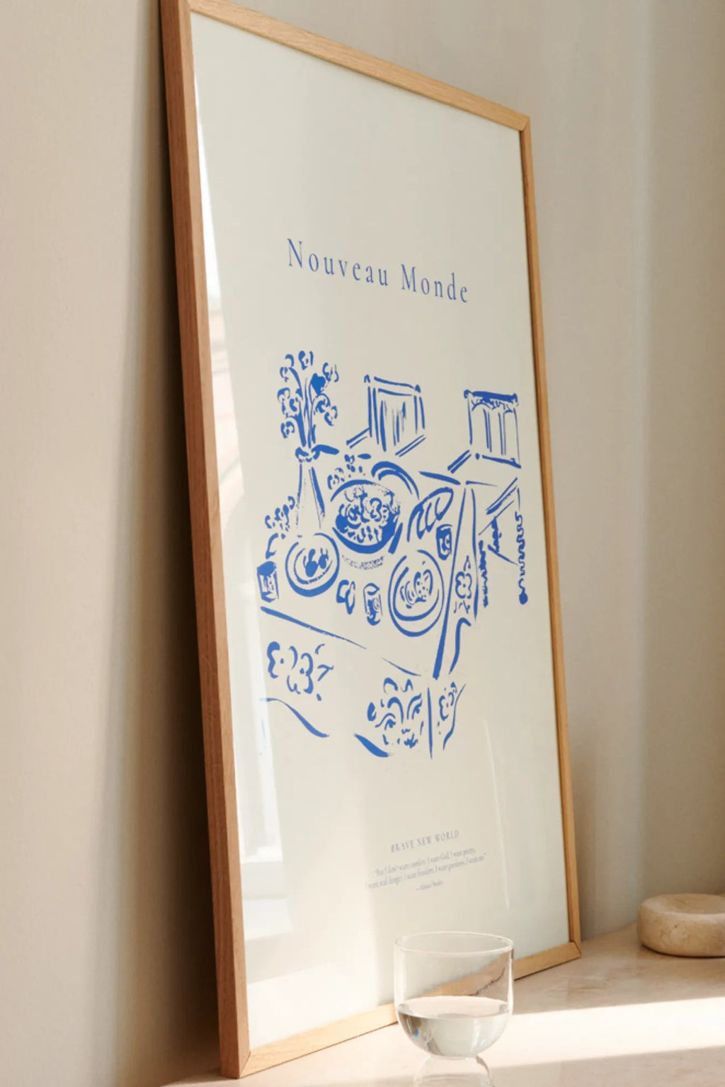 The Poster Club Nouveau Monde, a minimalist abstract art print featuring a vibrant royal blue line art illustration of a dining scene on a crisp white background, encased in a sleek natural oak frame. This contemporary poster is perfect as modern wall art for Scandinavian living rooms or a stylish addition to any gallery wall.