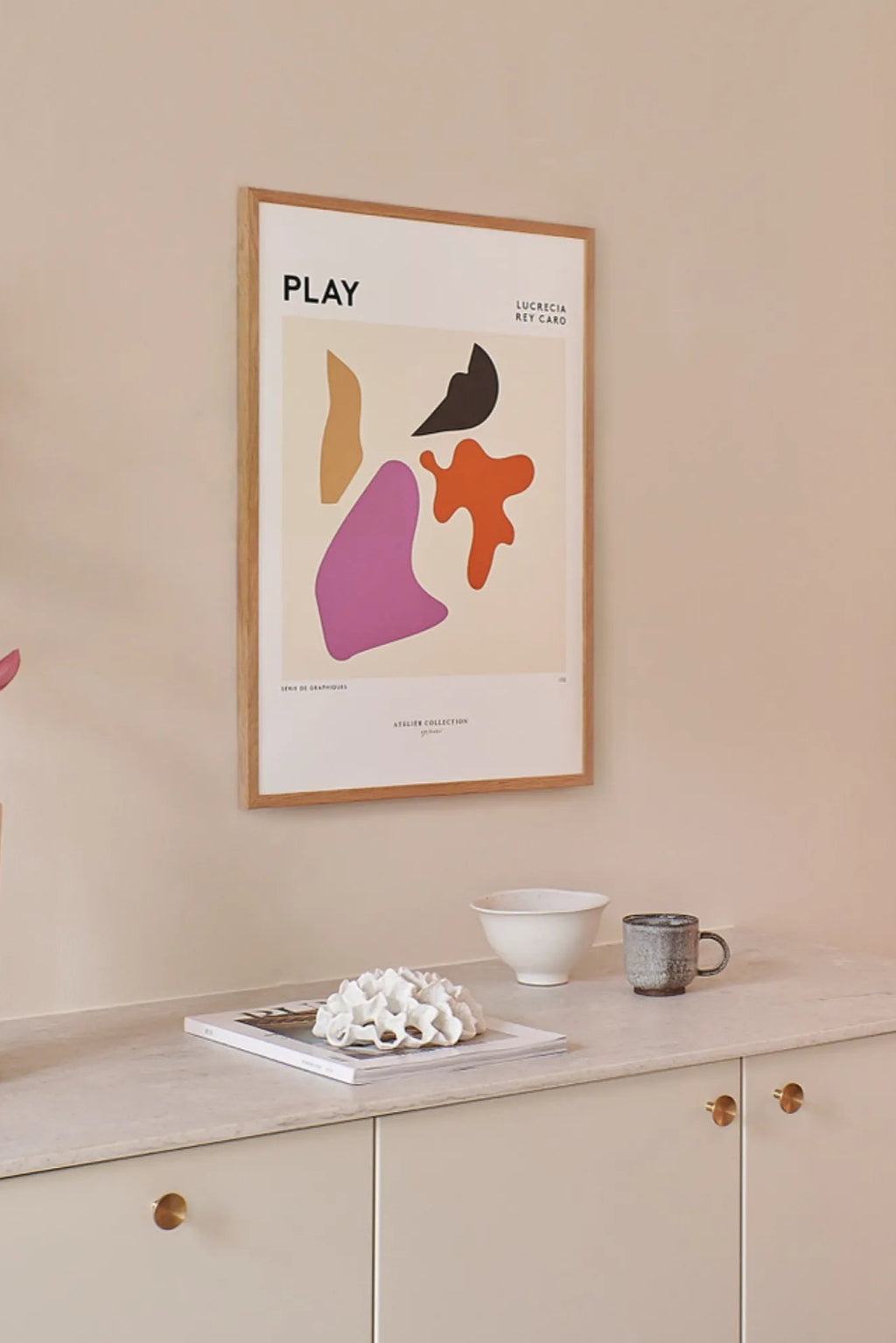 The Poster Club Play, a modern abstract art print by Lucrecia Rey Caro featuring bold, organic shapes in black, orange, purple, and tan against a cream background. This contemporary wall art is elegantly presented in a natural oak frame with a crisp white mat. It's an ideal piece for minimalist living rooms, modern gallery walls, or stylish home office decor.