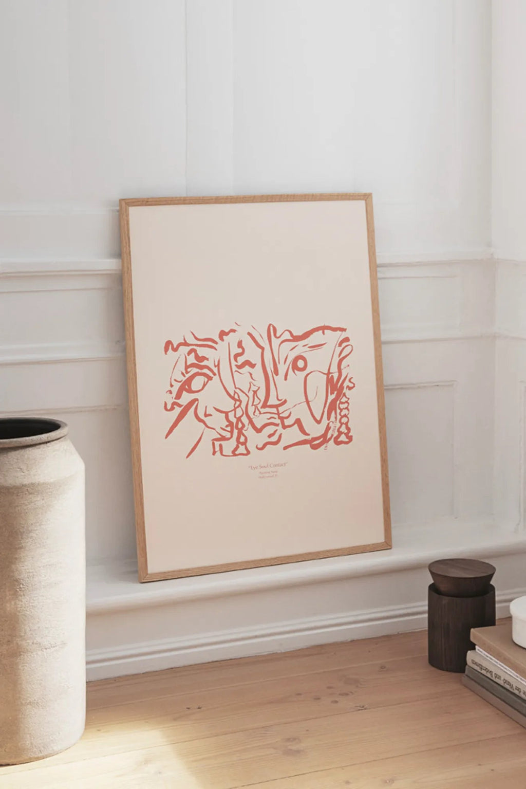 The Poster Club Soul Contact 01, a contemporary abstract art print featuring organic, flowing terracotta red line art on a warm beige background, depicting intertwined faces or figures. It is elegantly presented in a light natural oak frame, enhancing its minimalist aesthetic. Perfect as modern wall art for a Scandinavian living room, a boho bedroom, or a curated gallery wall in organic modern interiors.