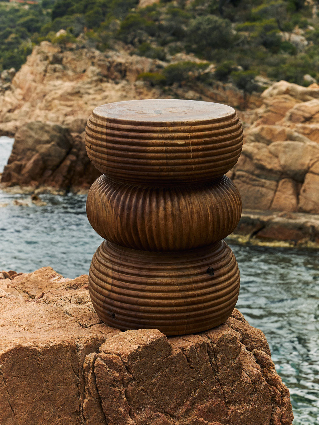 Heaps & Woods Luka Stool, a warm brown solid wood stool featuring a distinctive stacked, sculptural design with deeply carved horizontal ribbing. Each rounded segment creates an organic, tactile profile, showcasing the natural wood grain and handcrafted texture. Ideal as an organic modern side table, rustic accent stool, or sculptural decor for living rooms, bedrooms, or covered outdoor spaces.