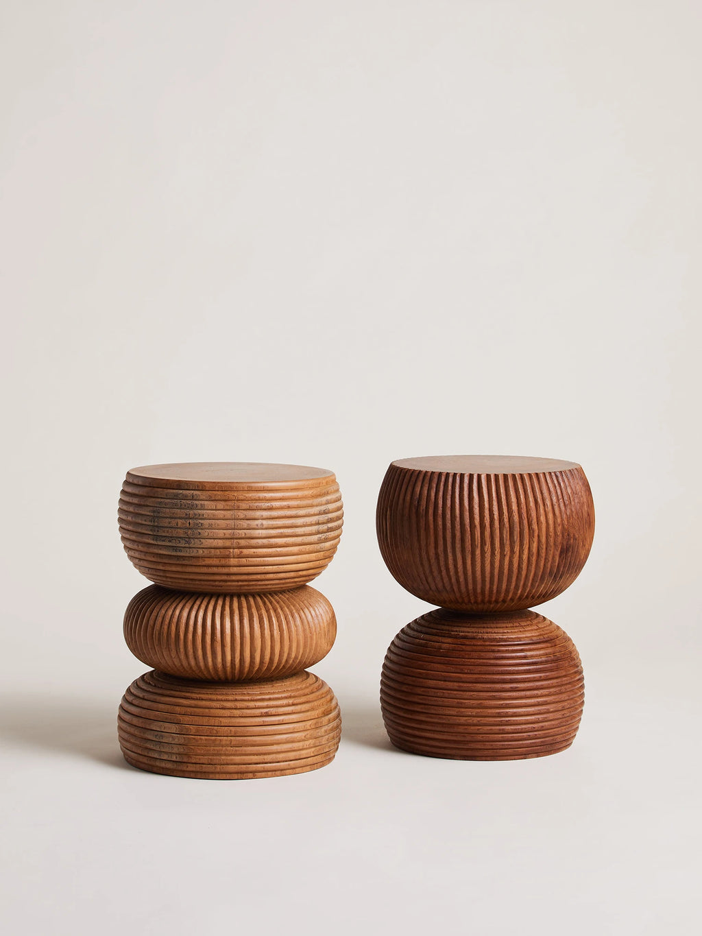 Heaps & Woods Luka Stool, a pair of hand-carved solid wood stools showcasing unique fluted and ribbed textures in warm natural brown tones, each with a distinct sculptural, stacked cylindrical form.