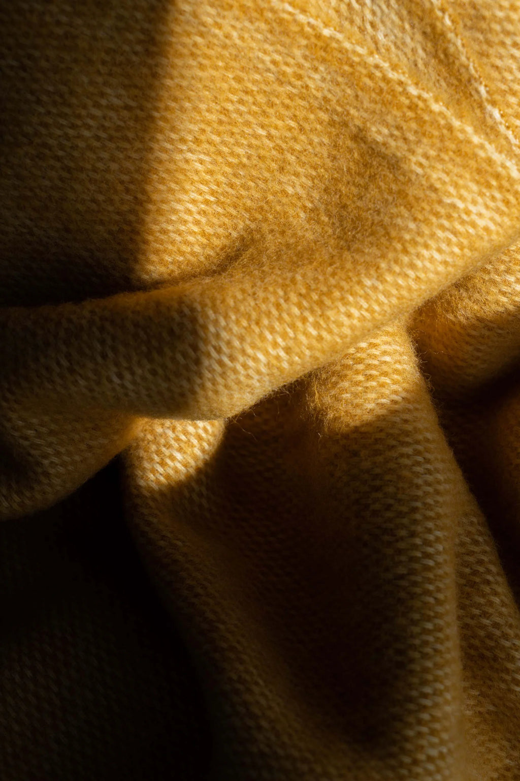 TAMO Meri Blanket Throw in warm mustard yellow, featuring a visible fuzzy, knitted texture and subtle light patterns. This premium, woven throw is ideal for cozy home decor.