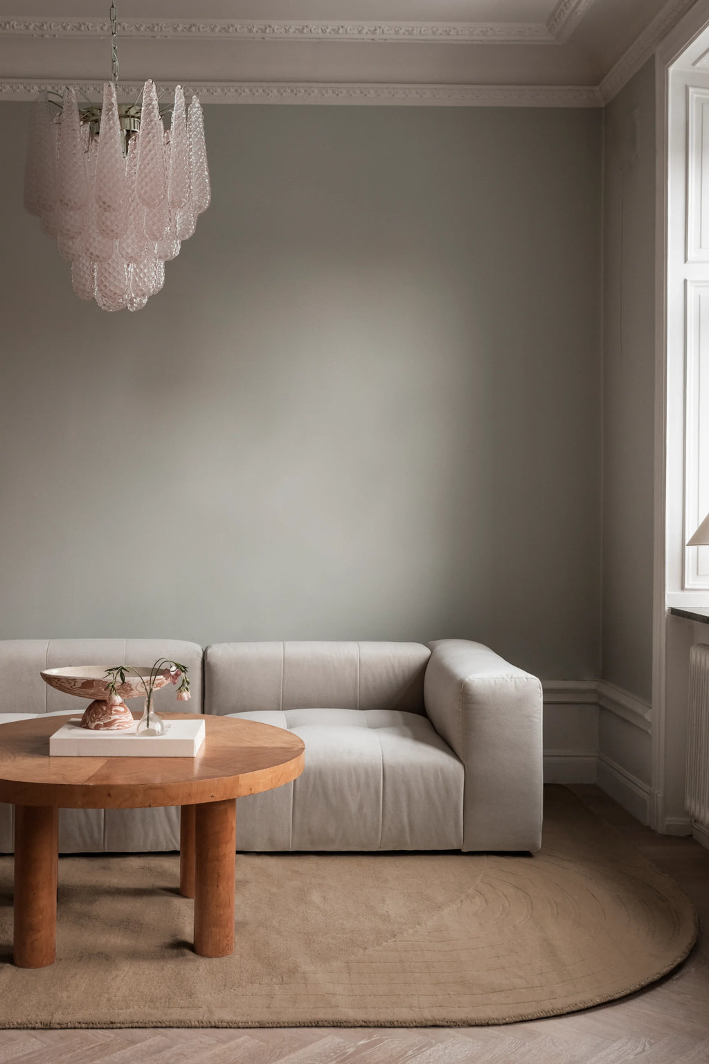 Layered Circular Wool Rug, a plush, light brown wool area rug with subtle concentric textured lines, partially visible under a light sofa and wooden coffee table. Perfect for adding warmth and soph...