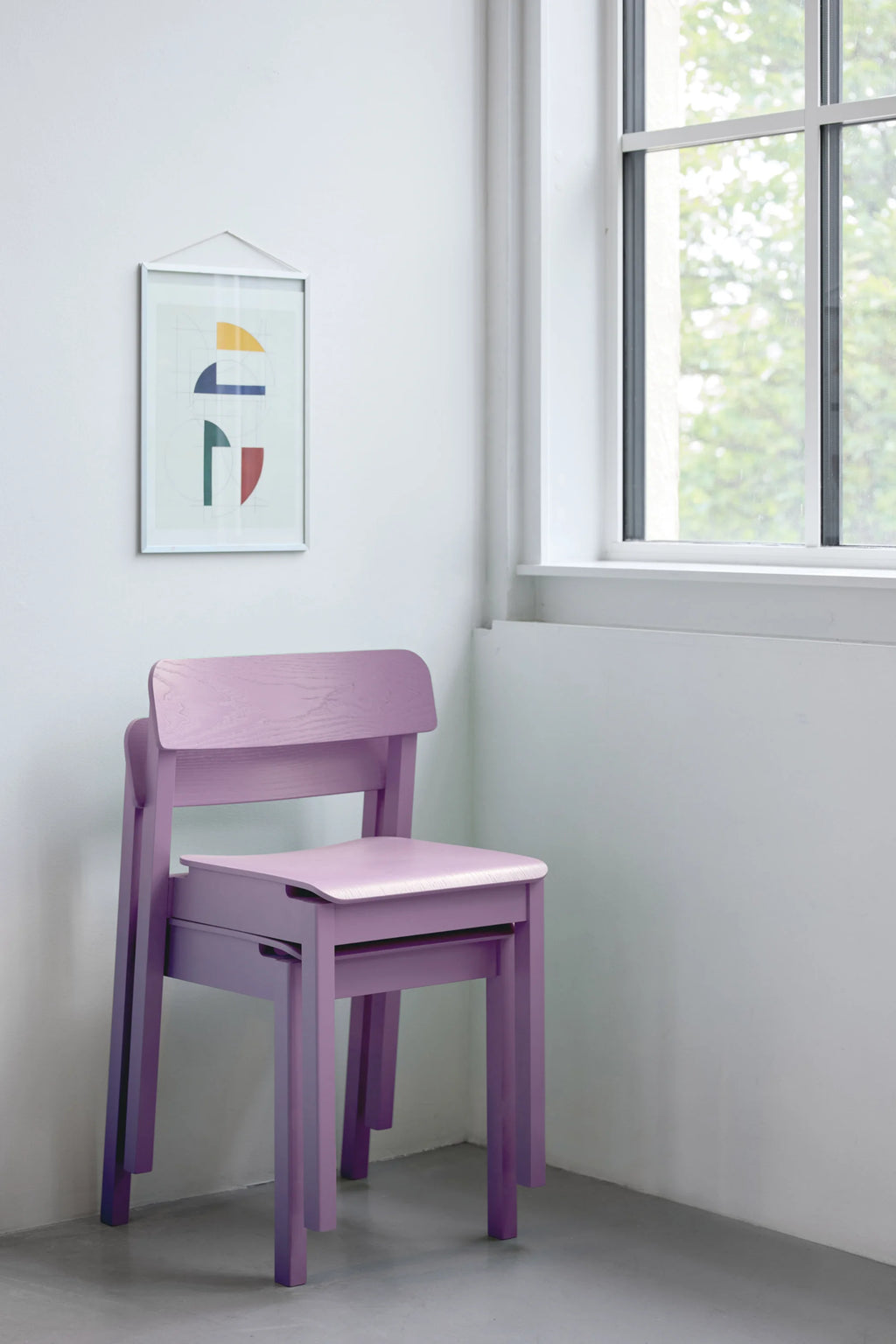 MOEBE Everyday Chair, a set of two minimalist stackable chairs crafted from light purple painted wood, featuring a subtle visible wood grain texture for an organic touch. The functional Scandinavian design boasts clean lines, a gently curved backrest, and a contoured seat, with one chair elegantly stacked on top of the other. Perfect as modern dining chairs or versatile accent seating for contemporary kitchens and Nordic-inspired spaces.