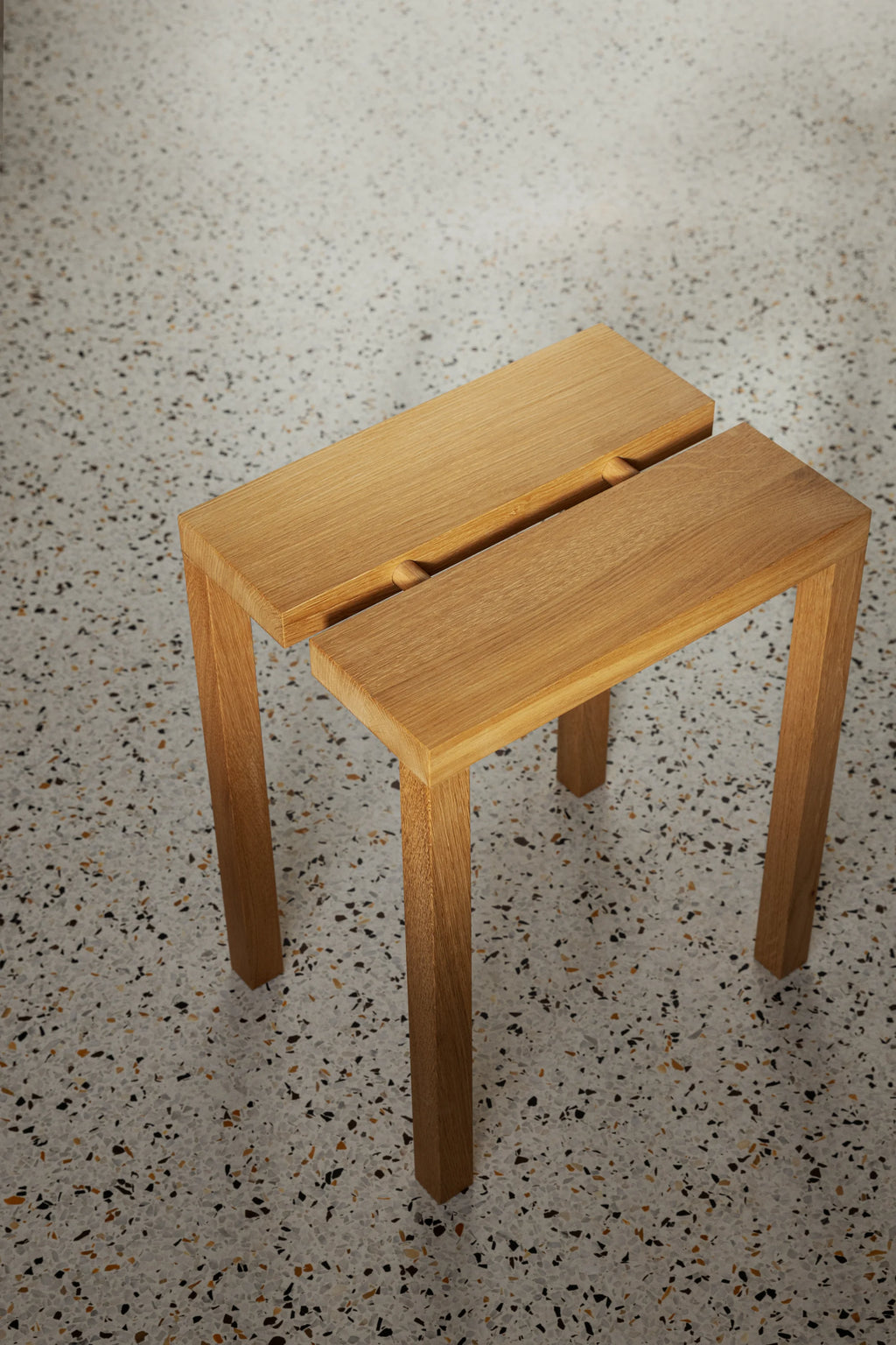 MOEBE Peg Stool, a modern minimalist solid oak stool crafted from light natural wood with visible grain texture. Its distinctive design features a split rectangular top connected by two round oak pegs in a central groove, resting on four sleek, straight legs for a clean Scandinavian aesthetic. Ideal as versatile seating, an accent piece, or a side table for contemporary living rooms, entryways, or minimalist bedrooms.