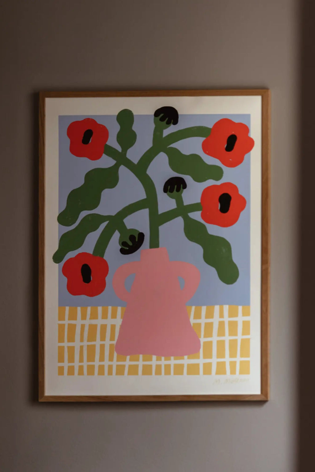 The Poster Club Red Poppies in Pink Vase, a vibrant abstract floral art print featuring bold red poppies with green stems and leaves in a soft pink vase against a light blue background, grounded by a cheerful yellow grid pattern. This modern graphic poster comes framed in a light natural oak frame with a crisp white mat, ideal for contemporary gallery walls, Scandinavian bedrooms, or playful kids' room decor.