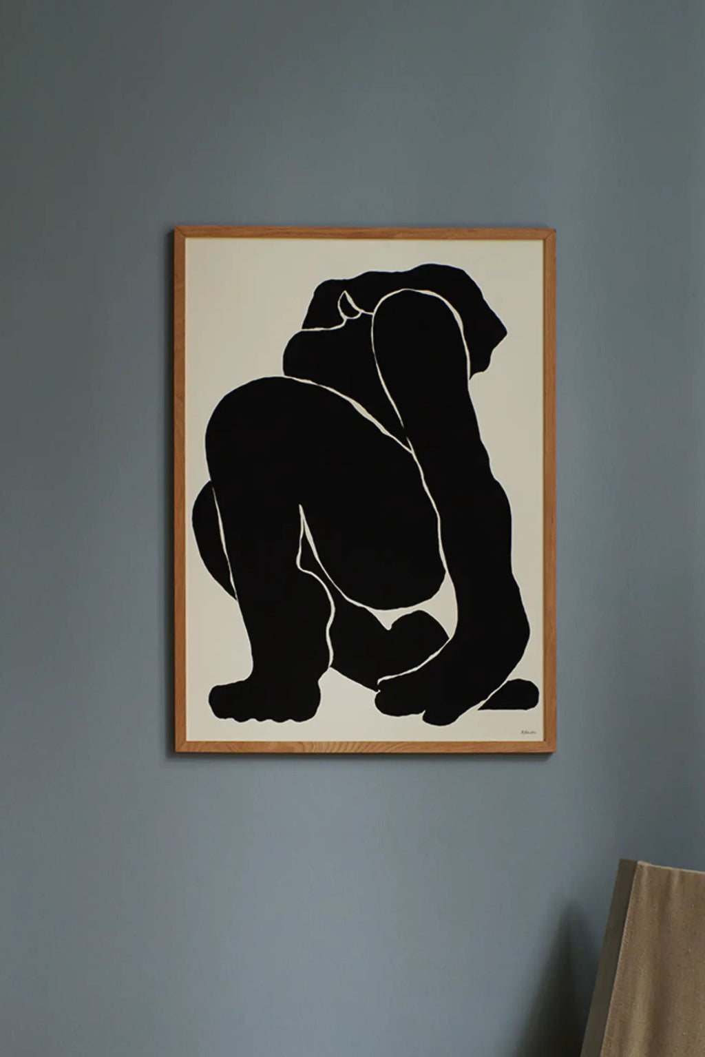 The Poster Club Slowly, an abstract minimalist poster featuring a squatting human figure rendered in bold black shapes with subtle white outlines against a warm off-white background. This contemporary figure drawing is presented in a light natural oak frame, enhancing its organic modern aesthetic. Ideal for creating a sophisticated focal point in a modern living room, bedroom, or gallery wall.
