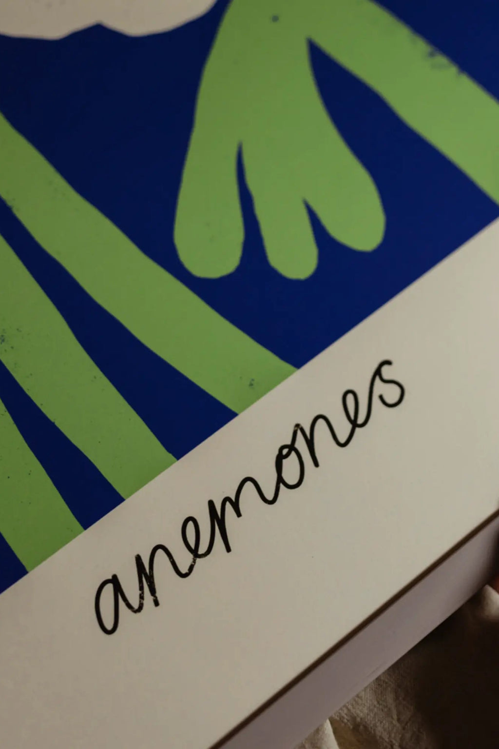 The Poster Club Yellow Anemones, a vibrant contemporary art print featuring bold, organic lime green shapes reminiscent of leaves or petals against a deep royal blue background, with the word "anemones.