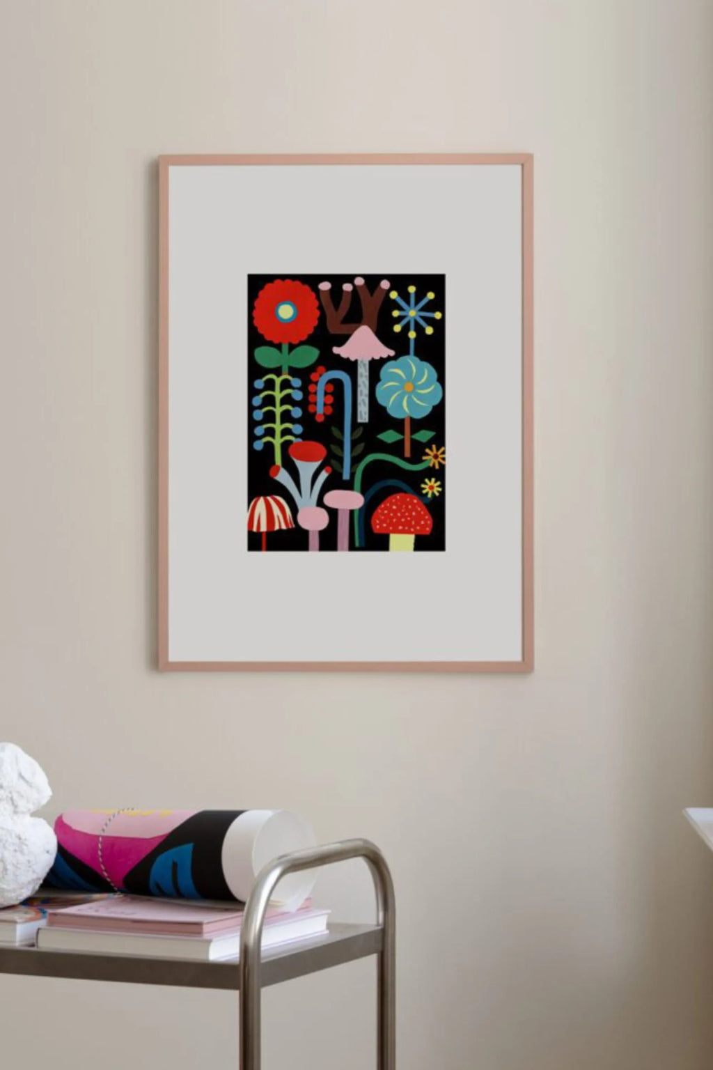 The Poster Club The Garden of the Night, a vibrant multi-colored abstract folk art print featuring whimsical botanical and mushroom motifs in red, blue, green, pink, and yellow against a deep black background. This playful wall art is presented in a modern light wood frame with a crisp white mat. Perfect as colorful art for a nursery, kids room, or a mid-century modern living room gallery wall.
