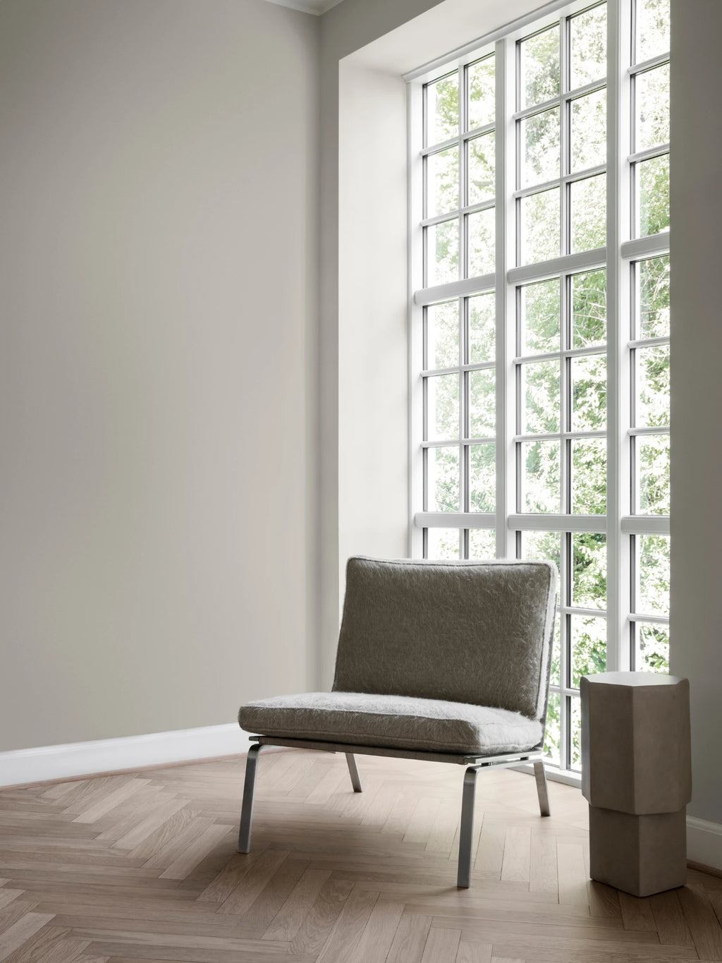 NORR11 Man Lounge Chair, a modern minimalist lounge chair featuring soft grey felted wool upholstery on a low-slung, rectangular seat and backrest. It sits on a sleek polished stainless steel frame with clean lines, embodying a Scandinavian contemporary design. Ideal as an accent chair for a modern living room, bedroom, or cozy reading nook.