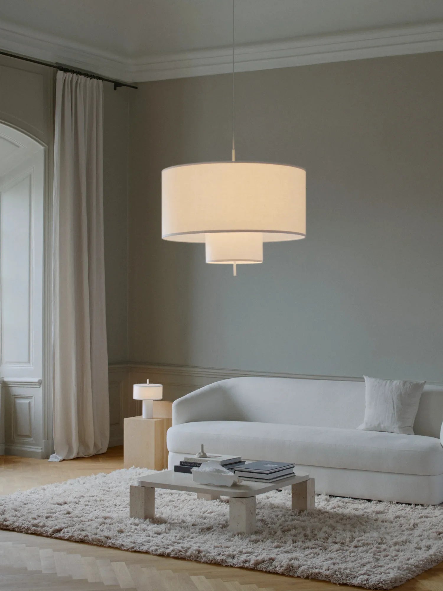 New Works Margin Pendant Lamp with a multi-tiered cream textile shade suspended in a minimalist living room. The large, modern ceiling fixture provides soft, inviting ambient light.
