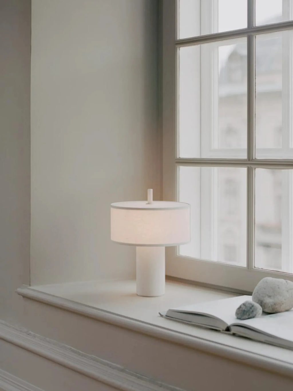 New Works Margin Portable Table Lamp, an elegant white fabric dome shade and cylindrical base, casting a soft glow. A premium, minimalist design perfect for modern interiors.