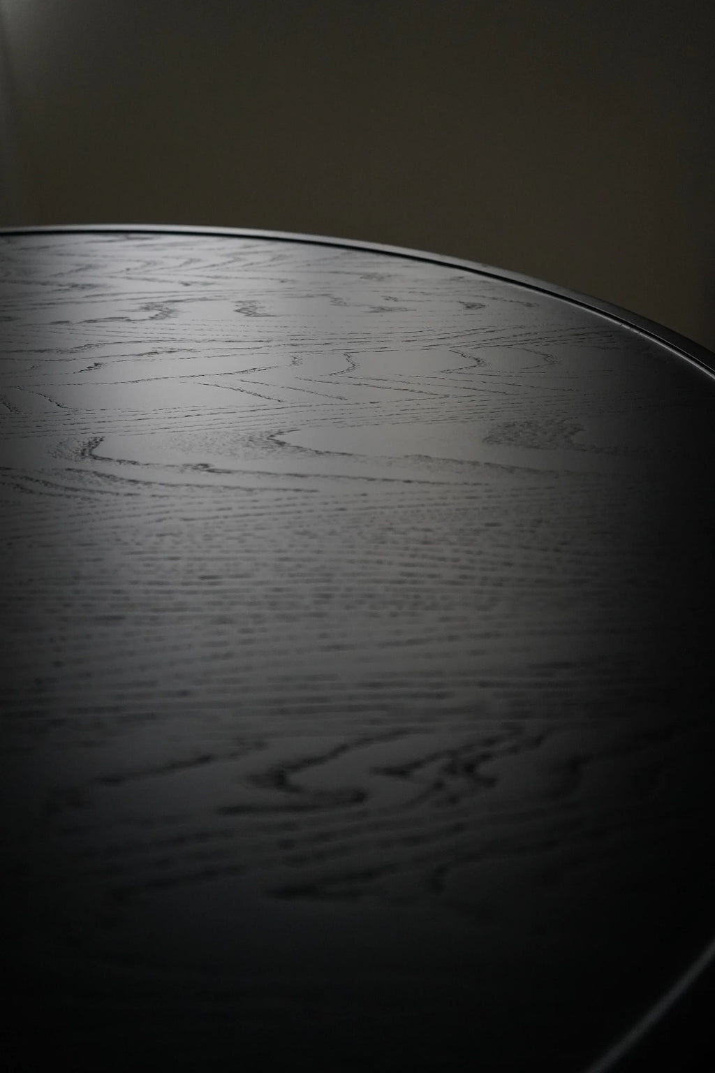 Mater Accent Round Dining Table, showcasing the rich, dark stained oak wood grain texture on the smooth, elegant tabletop, subtly reflecting light, displayed on a dark, minimalist background.