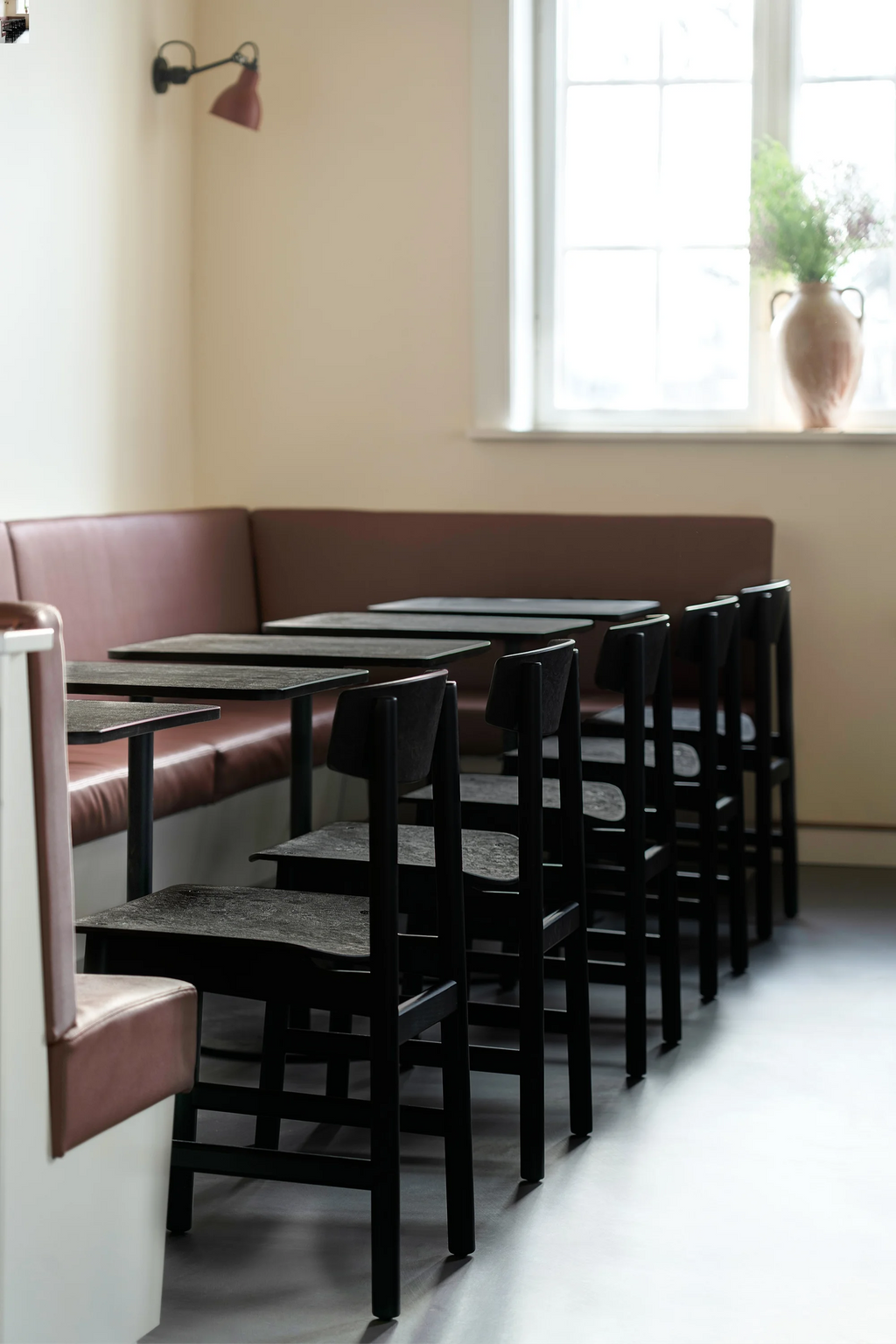 Mater Conscious Chair in black coffee waste black, a row of modern, dark chairs with textured seats and backs, arranged neatly at tables in a stylish cafe setting with a window.