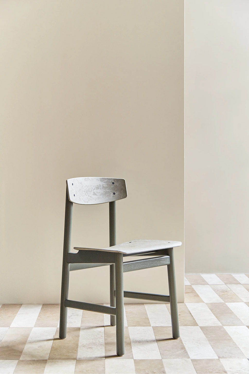 Mater Conscious Chair in a coffee green stained oak finish, featuring a light green, subtly textured seat and backrest, positioned elegantly against a warm beige wall and tiled floor.