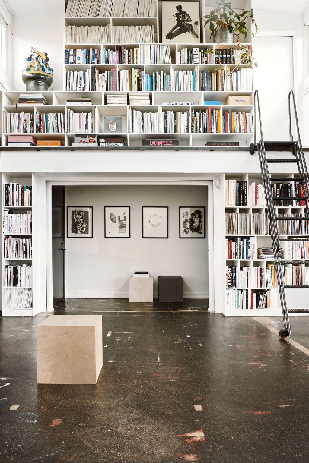 Mater Cube, two stylish cube-shaped side tables in light beige and dark brown, with subtle textured patterns, complementing a large, modern library space with extensive bookshelves.