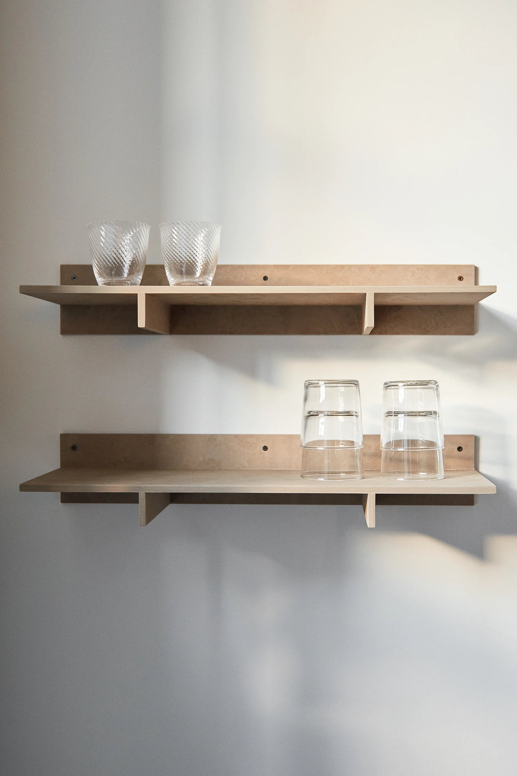Mater Edge Shelf in a light, natural wood finish, a pair of modern wall-mounted shelves, elegantly displaying clear textured glasses, adding functional and aesthetic appeal to any room.