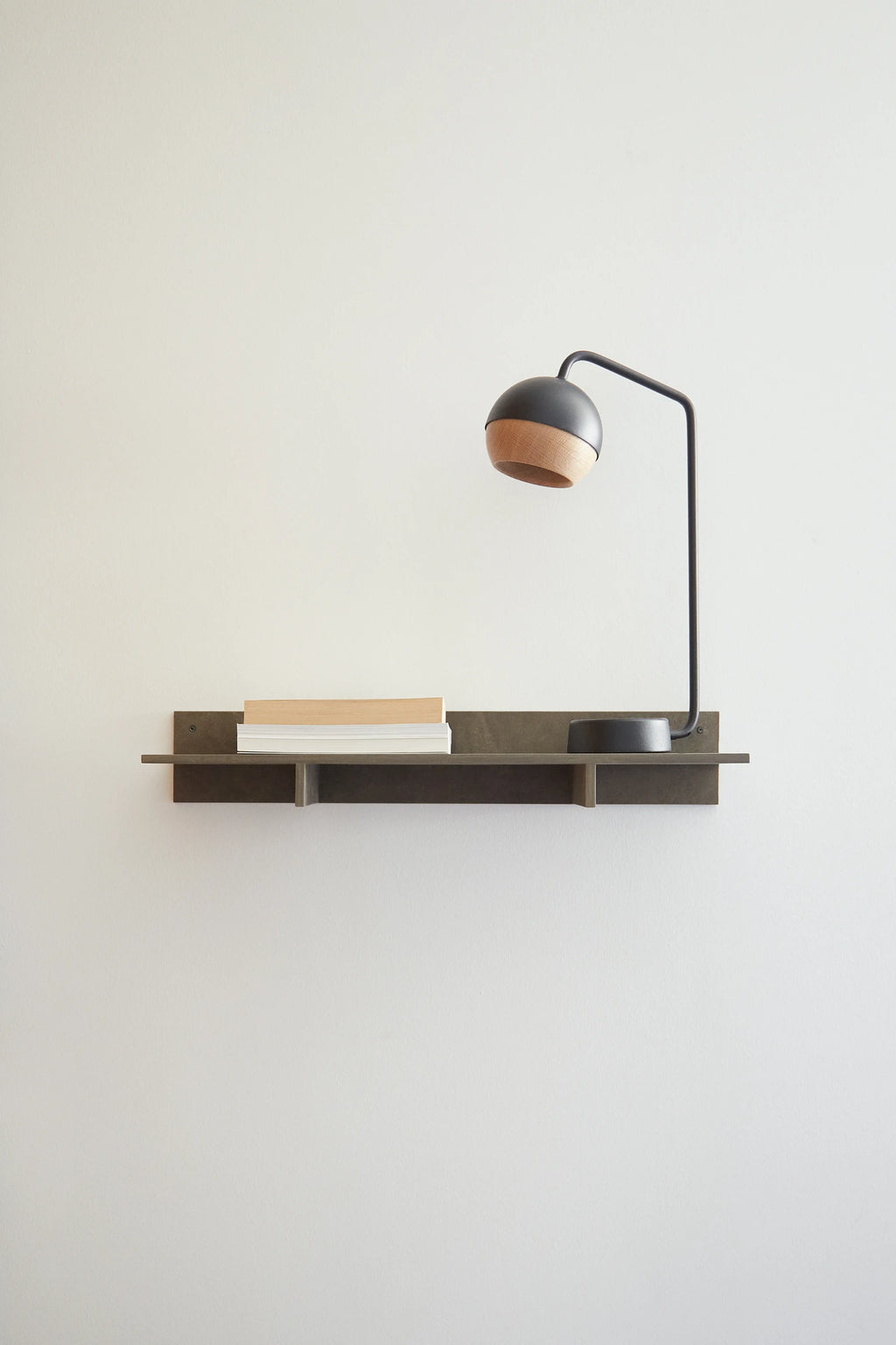 Mater Edge Shelf in a dark, elegant wood finish, a contemporary wall-mounted shelf featuring a unique design, styled with a modern black and cork lamp and books in a minimalist interior.