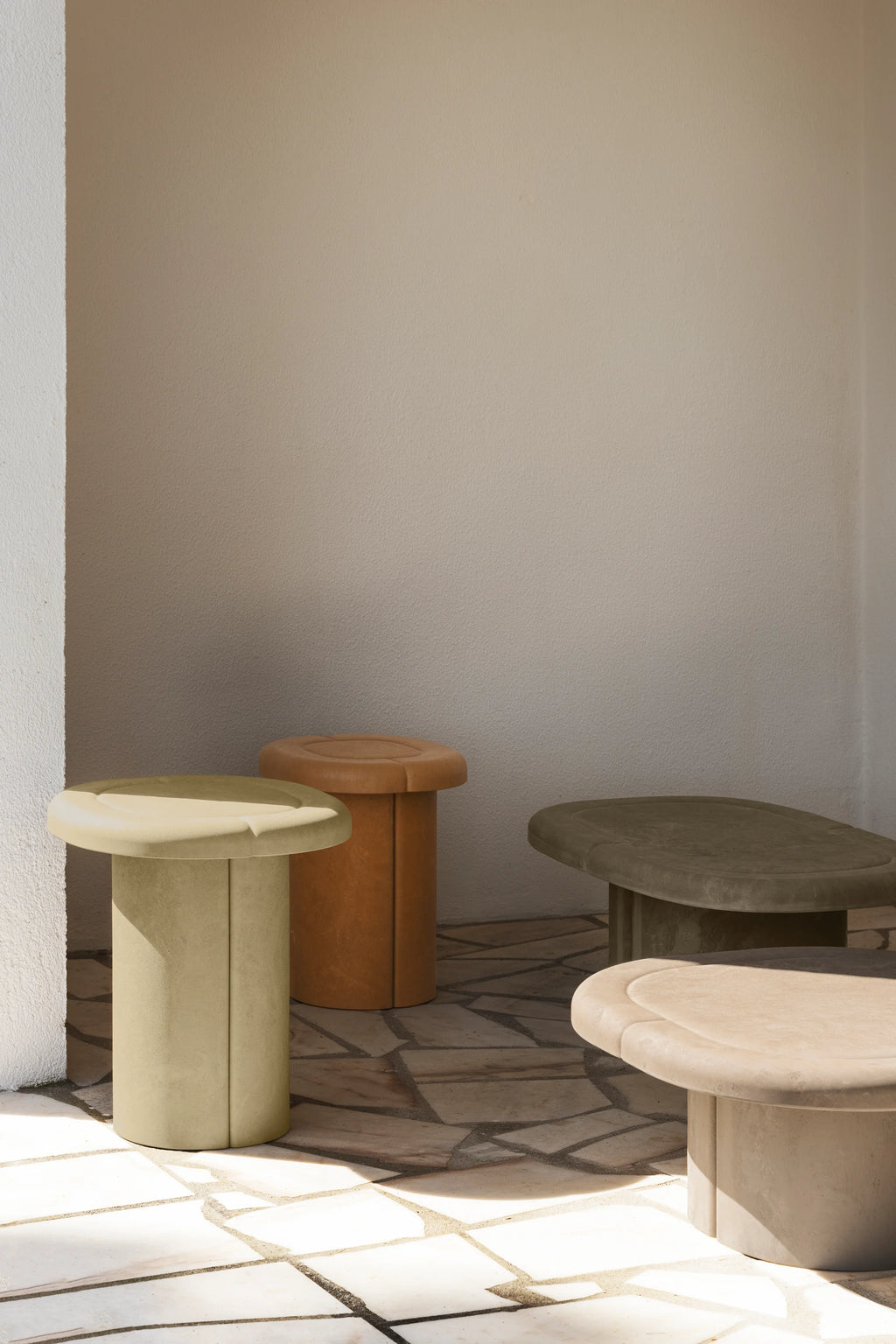 Mater Alder Coffee Table collection, featuring multiple organic-shaped tables in varying earthy tones like light green, terracotta, and beige, with soft, rounded edges, displayed on a tiled outdoor patio.