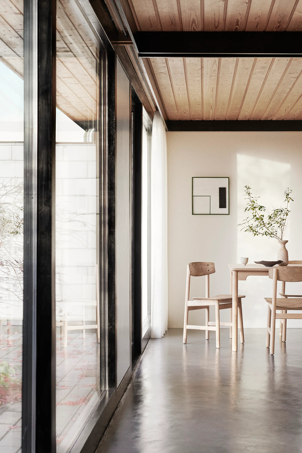Mater Conscious Chair in natural light oak, part of a dining set in a bright, modern room with large windows. The chair's minimalist design and light wood tones contribute to a serene and open living space, highlighting its sustainable craftsmanship.