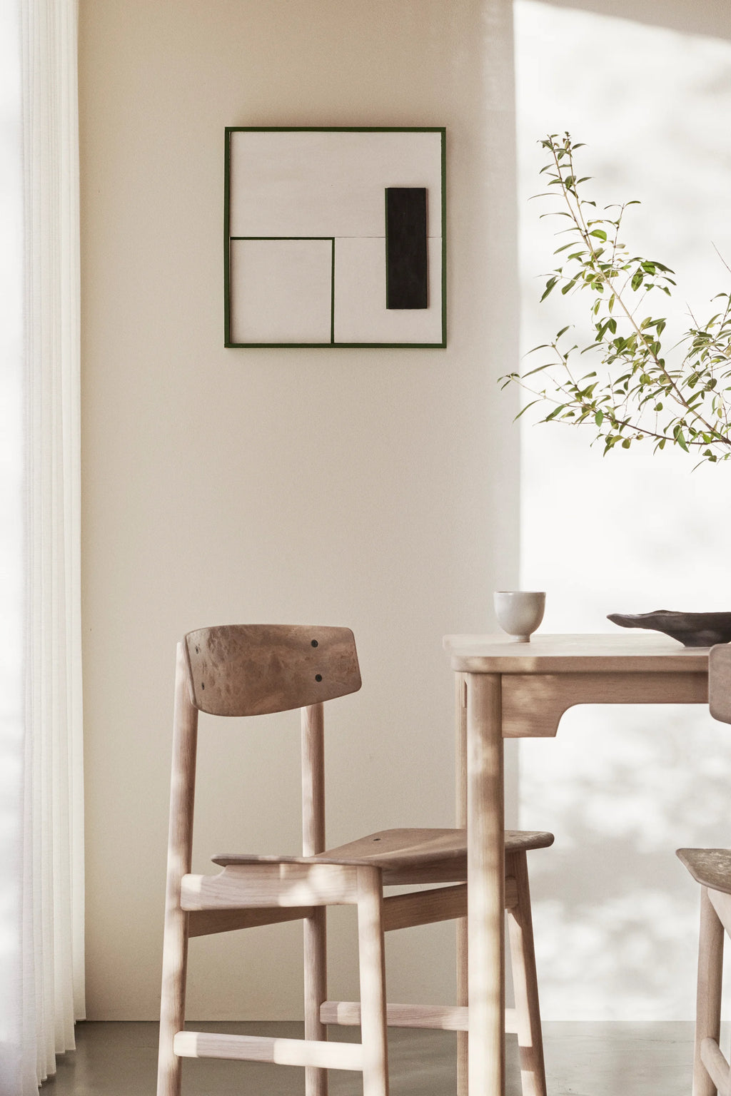 Mater Conscious Chair in natural light oak, positioned beside a matching wooden dining table in a sunlit room. The chair's organic form and light wood grain create a warm, inviting atmosphere, enhancing the modern decor.