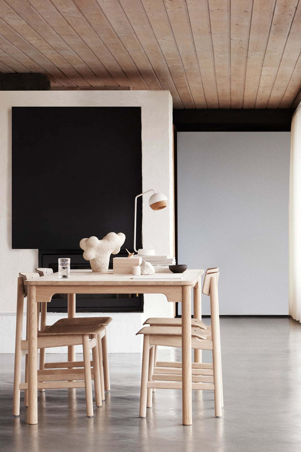 Two Mater Conscious Chairs in natural light oak, arranged around a dining table in a spacious, modern room. The chairs' clean lines and light wood finish create an airy feel, complementing the wooden ceiling and minimalist decor.