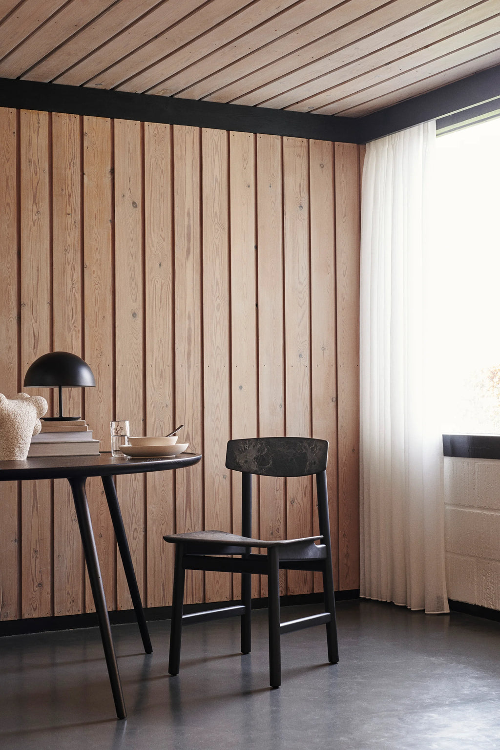 Mater Conscious Chair in a dark, charcoal finish, paired with a round black dining table in a stylish room. The chair's recycled plastic seat and backrest, combined with its solid frame, create a sophisticated and sustainable dining solution.
