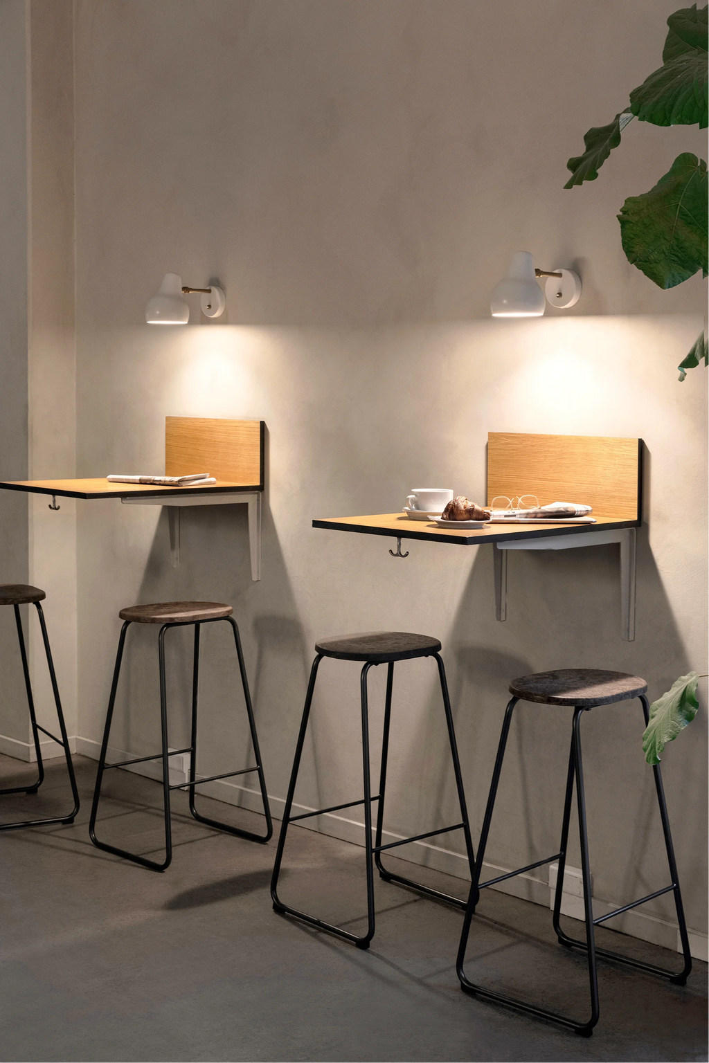 Mater Earth Counter Stool, a contemporary, backless design featuring a dark brown recycled composite seat and robust black metal legs, set in a stylish cafe environment with wooden wall tables.