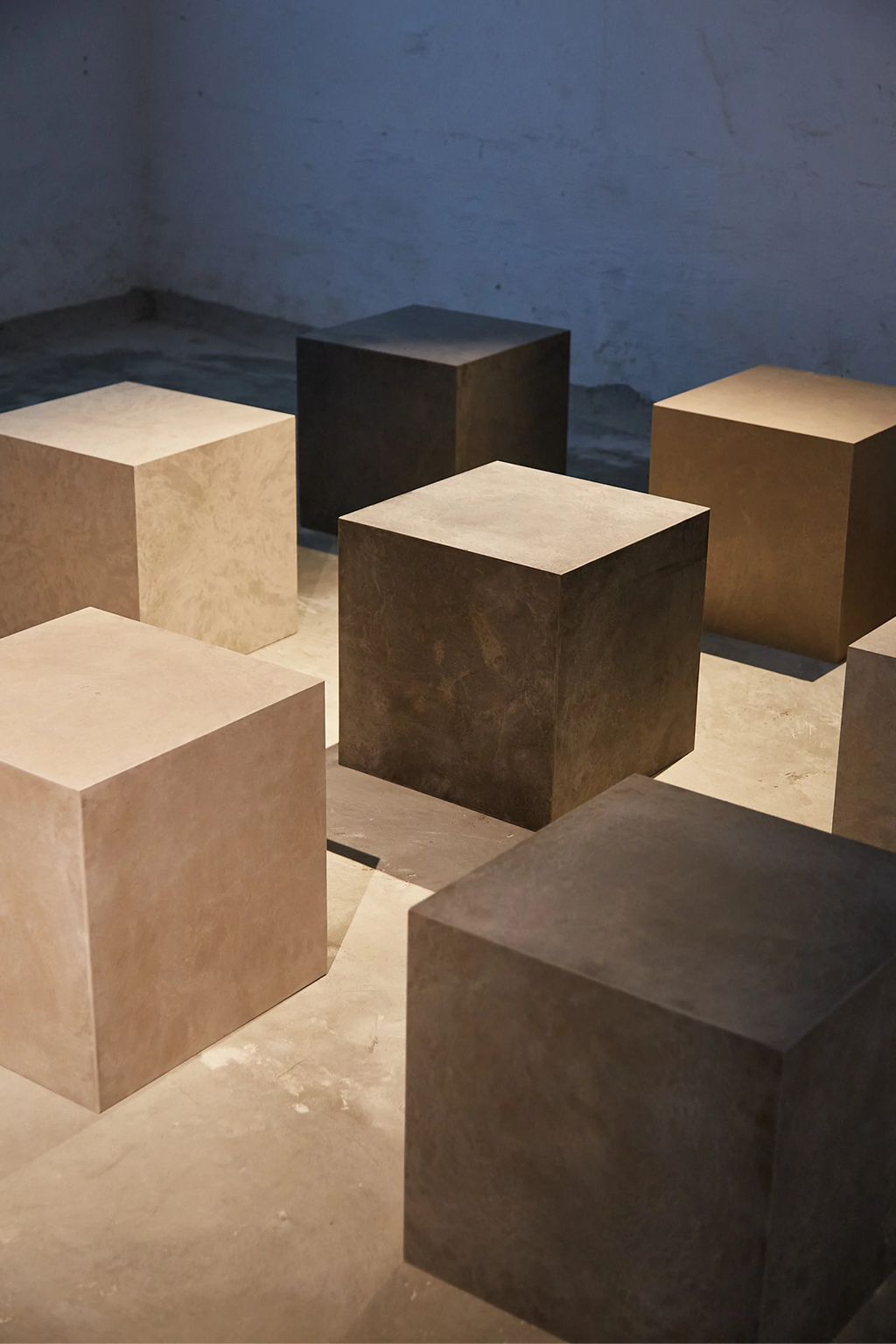Mater Cube, multiple contemporary cube-shaped side tables in varying shades of dark brown and light beige, exhibiting a sophisticated, textured finish, arranged in a spacious, modern interior.