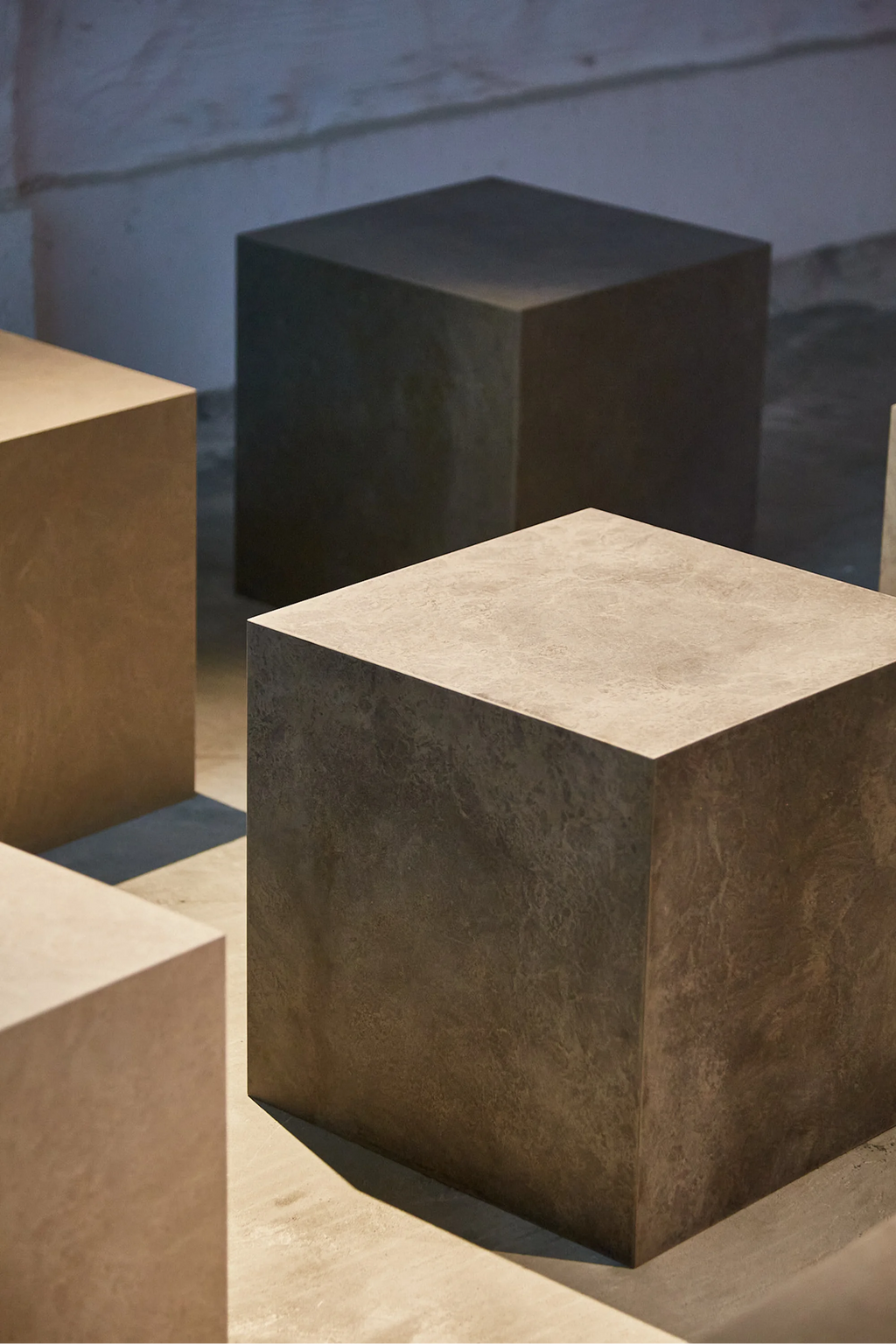 Mater Cube, a modern, minimalist cube-shaped side table or stool, showcasing its dark, textured surface with subtle variations, displayed in a dimly lit, contemporary setting.