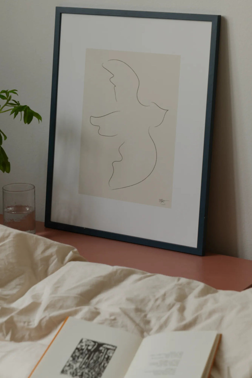 The Poster Club Fly Away, a minimalist abstract line art print featuring a delicate black figurative drawing on a light beige background, beautifully presented with a crisp white mat and a dark blue-grey wooden frame. This contemporary framed art is perfect for modern bedroom decor, minimalist living rooms, or elegant gallery wall styling.