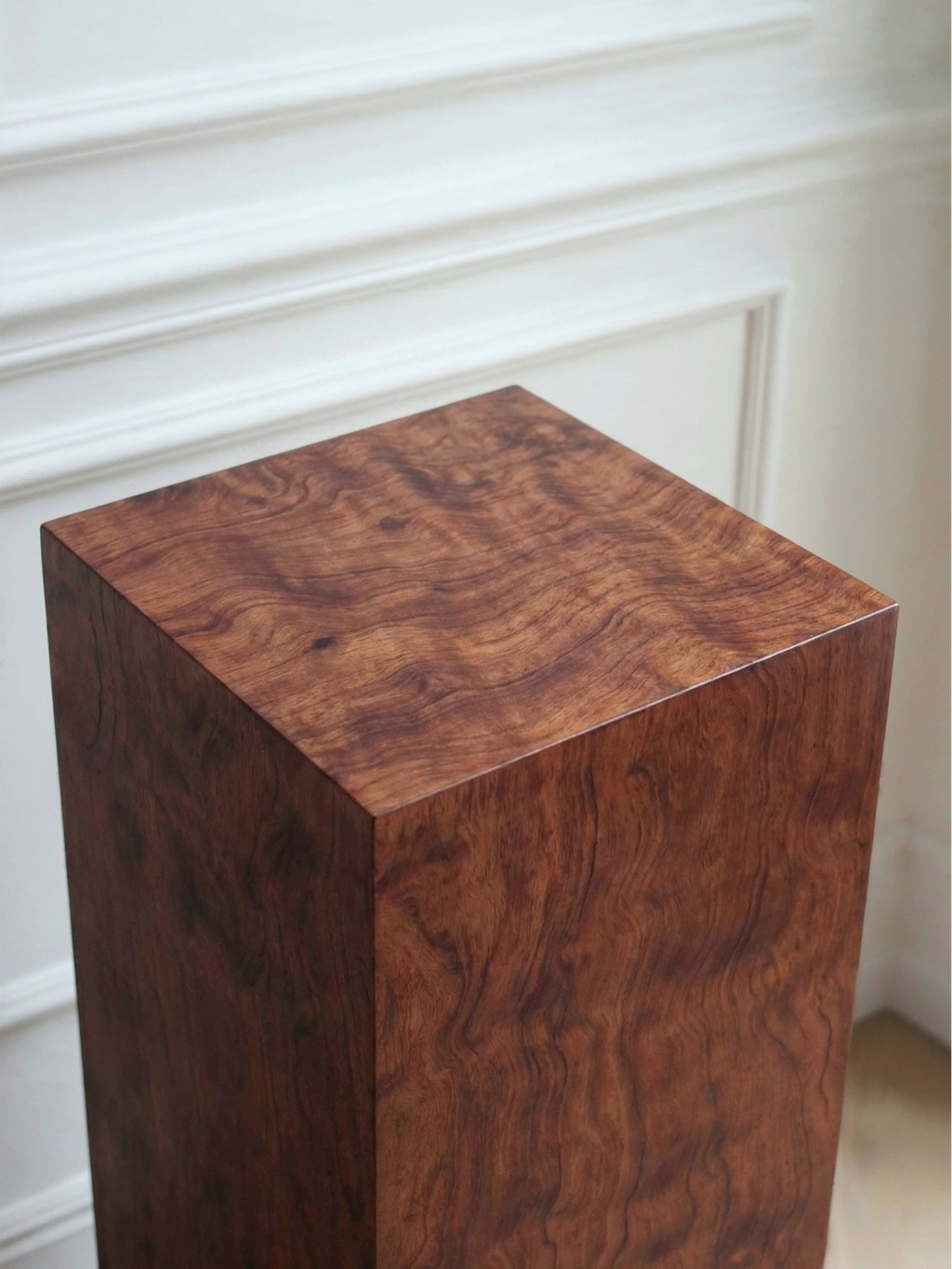 TCL Studios Monolith Pomele Display Column, a striking square column pedestal crafted from rich, dark pomele wood with a highly figured, wavy grain and a smooth, polished finish. This contemporary minimalist side table features deep reddish-brown tones and a luxurious organic wood pattern, creating a sophisticated statement piece. Perfect as a modern display column for art or plants, or a chic accent side table in luxury living rooms, entryways, or contemporary bedrooms.