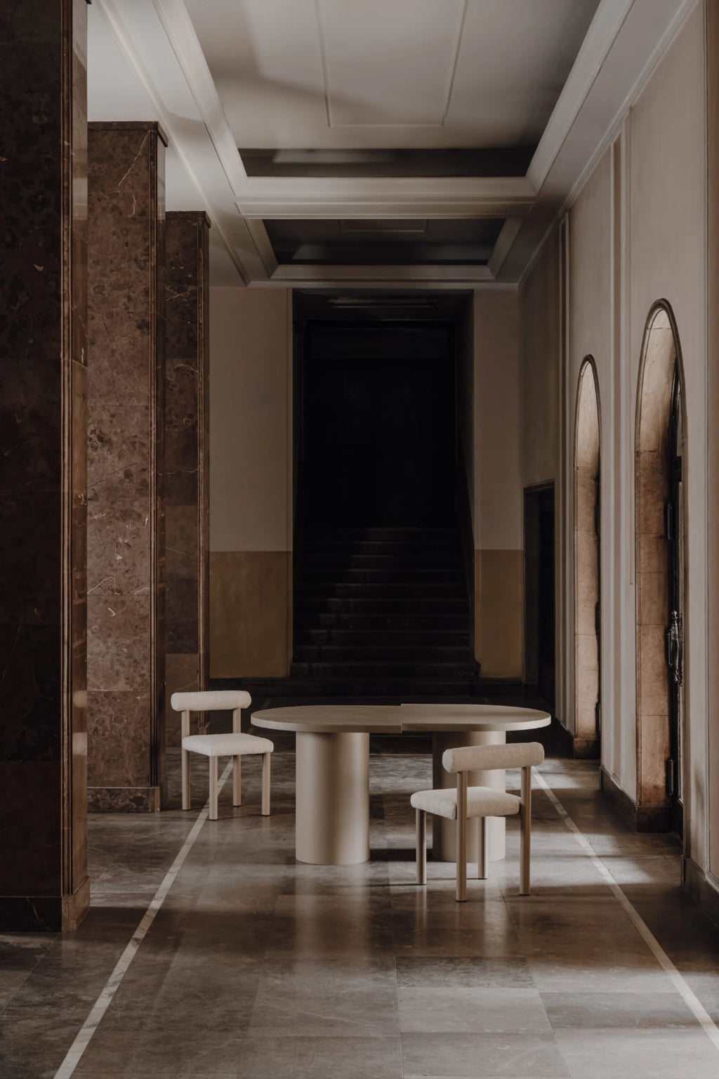 NG DESIGN Object 098 Dining Table, a luxurious, light beige round table with two thick cylindrical bases, displayed with two matching upholstered chairs in an elegant hall. Ideal for sophisticated interiors.