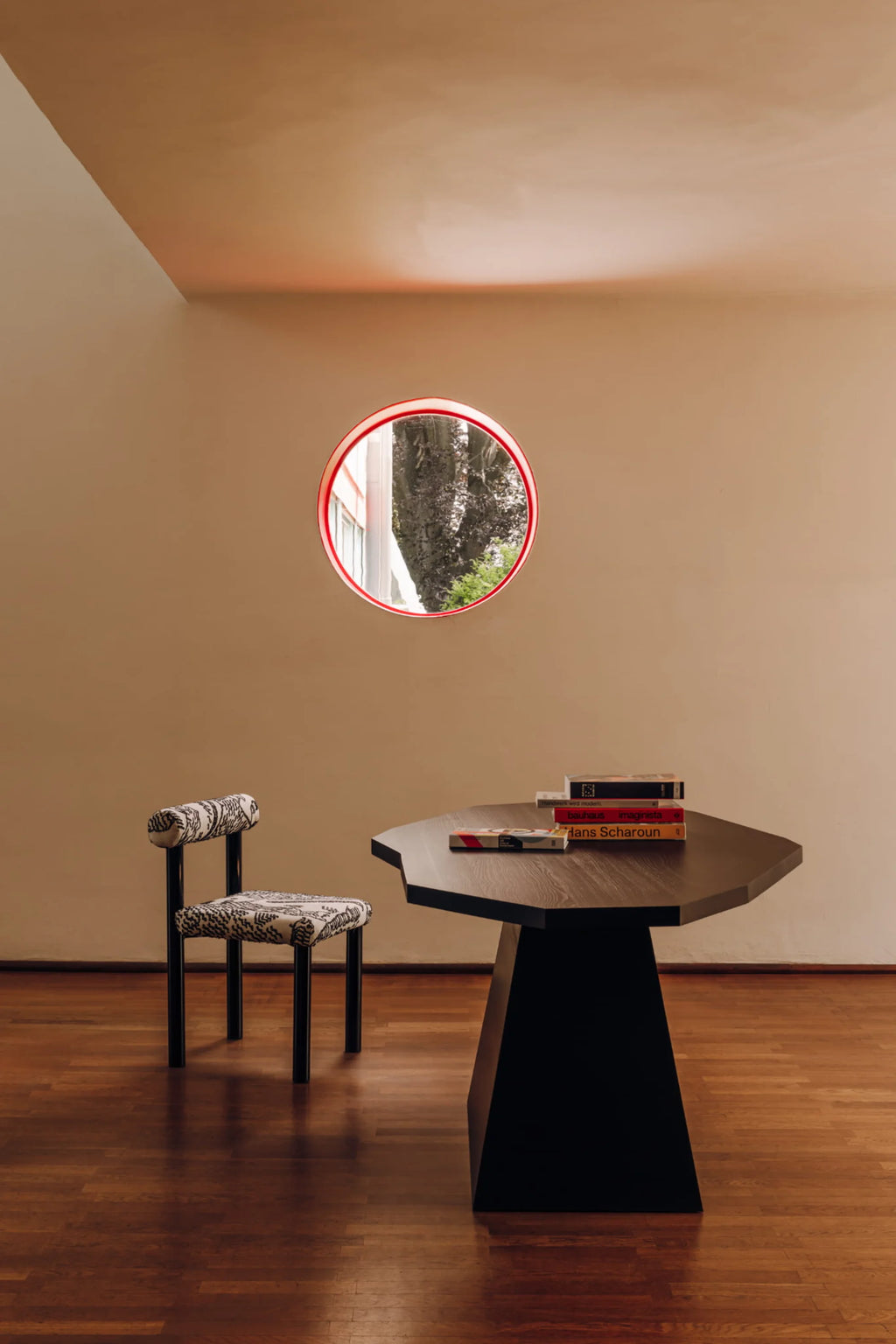 NG DESIGN's "Object 110 Dining Table" features a unique octagonal, dark brown wooden top and a solid black trapezoidal base, styled with books in a warm-toned room with wooden floors. A premium statement piece for modern dining.