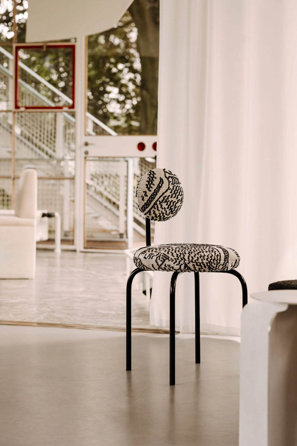NG DESIGN Object 077 Chair with a round back and seat, upholstered in a striking cream and black patterned fabric, featuring sleek black metal legs, displayed in a modern interior. This unique accent chair is ideal for contemporary living spaces.