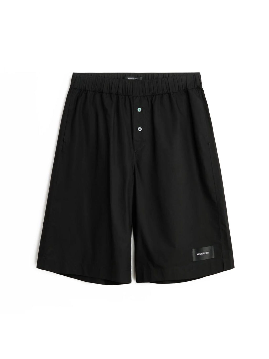 Magniberg Night shorts, a pair of black cotton shorts designed for ultimate comfort with a relaxed, wide-leg fit and a smooth matte fabric finish. These modern minimalist shorts feature a comfortable elasticated waistband and a functional button fly with subtle light blue buttons. Perfect as premium loungewear or sophisticated sleepwear for men seeking understated style.
