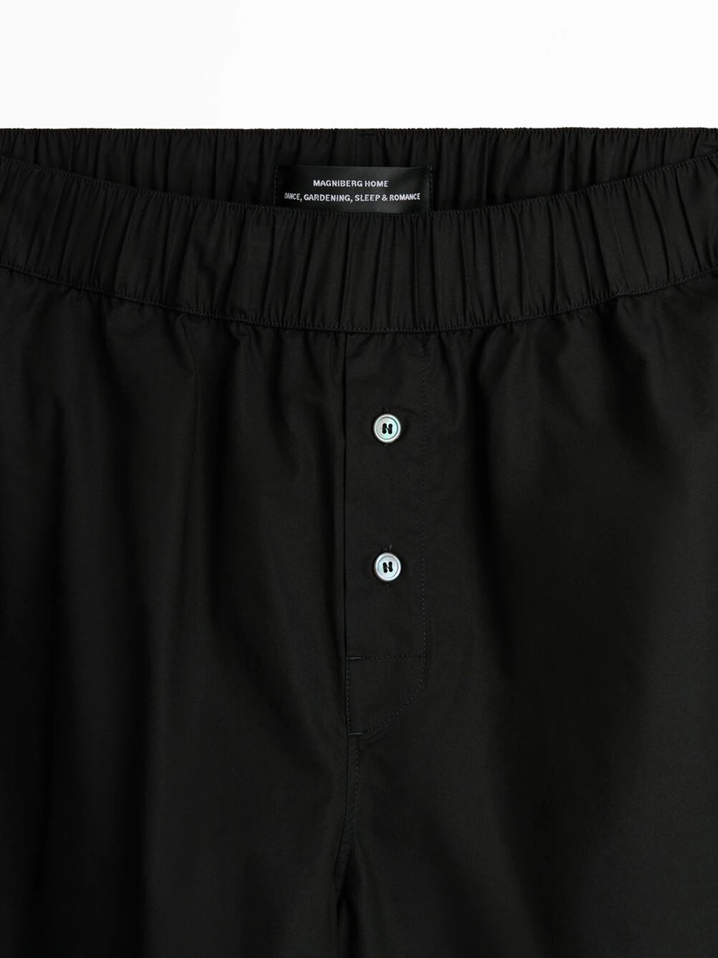 Magniberg Night shorts, a pair of black soft cotton lounge shorts featuring a comfortable elasticated waistband and a discreet button fly with contrasting white buttons. These modern minimalist sleep shorts are designed for luxurious relaxation and everyday comfort at home.