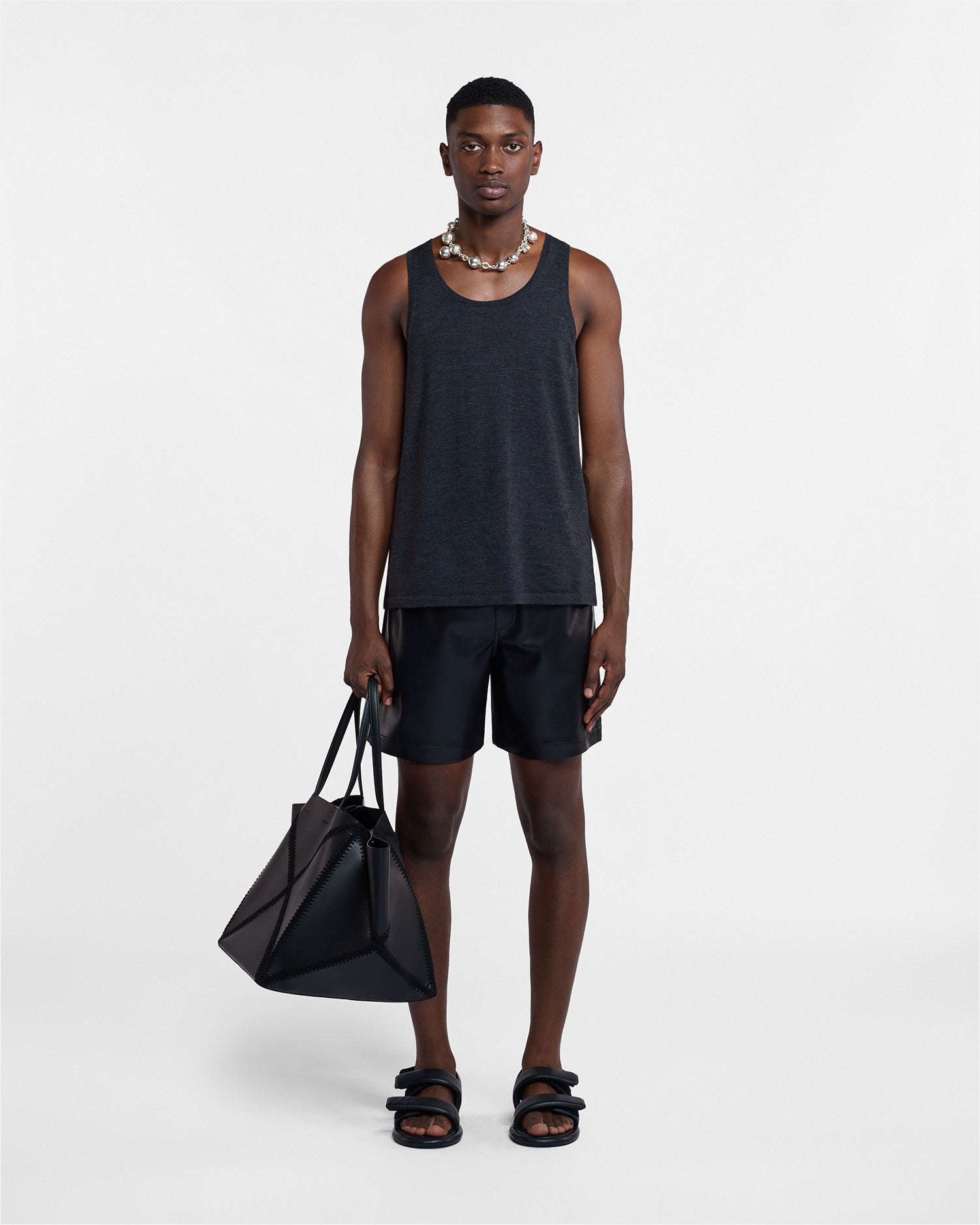 Man wearing a black tank top and shorts holding a black bag on a white background
