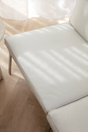 White leather chair on a wooden floor with sheer curtains in the background