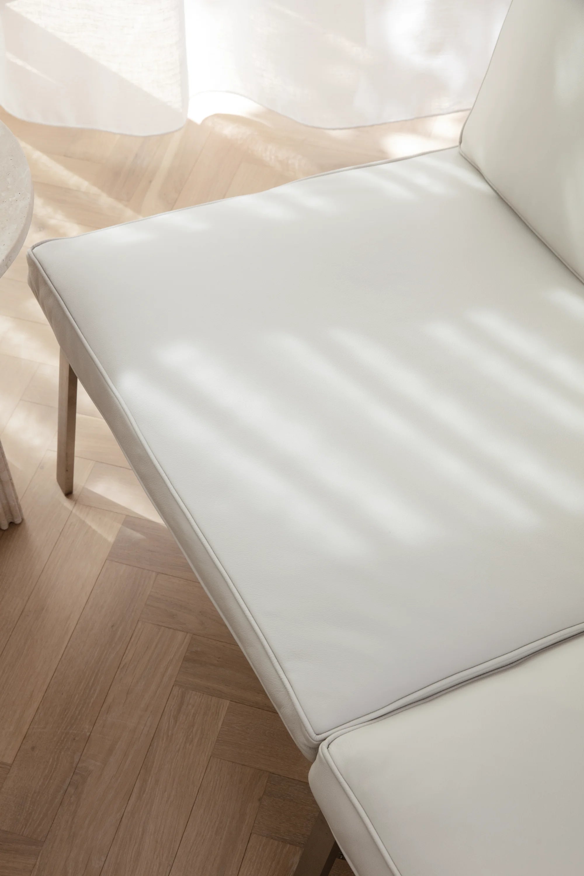 White leather chair on a wooden floor with sheer curtains in the background