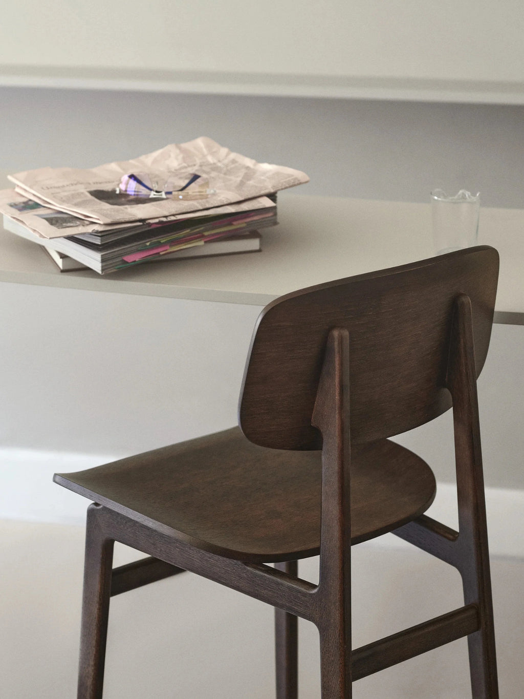 NORR11 NY11 Bar Chair, a dark stained solid oak bar chair with a minimalist Scandinavian design, featuring a subtly curved backrest and seat, and clean-lined angled legs. This contemporary wooden counter stool is perfect for modern kitchen islands, home bars, or stylish dining areas.