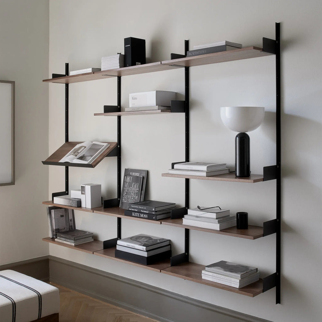New Works Display Shelf, a modern minimalist wall-mounted shelving unit featuring rich dark wood shelves (likely walnut veneer) supported by sleek matte black metal uprights and brackets. This contemporary modular bookshelf system includes various shelf depths and an angled display shelf, ideal for showcasing books and decor. Perfect for Scandinavian living rooms, home offices, or elegant display in any modern interior.