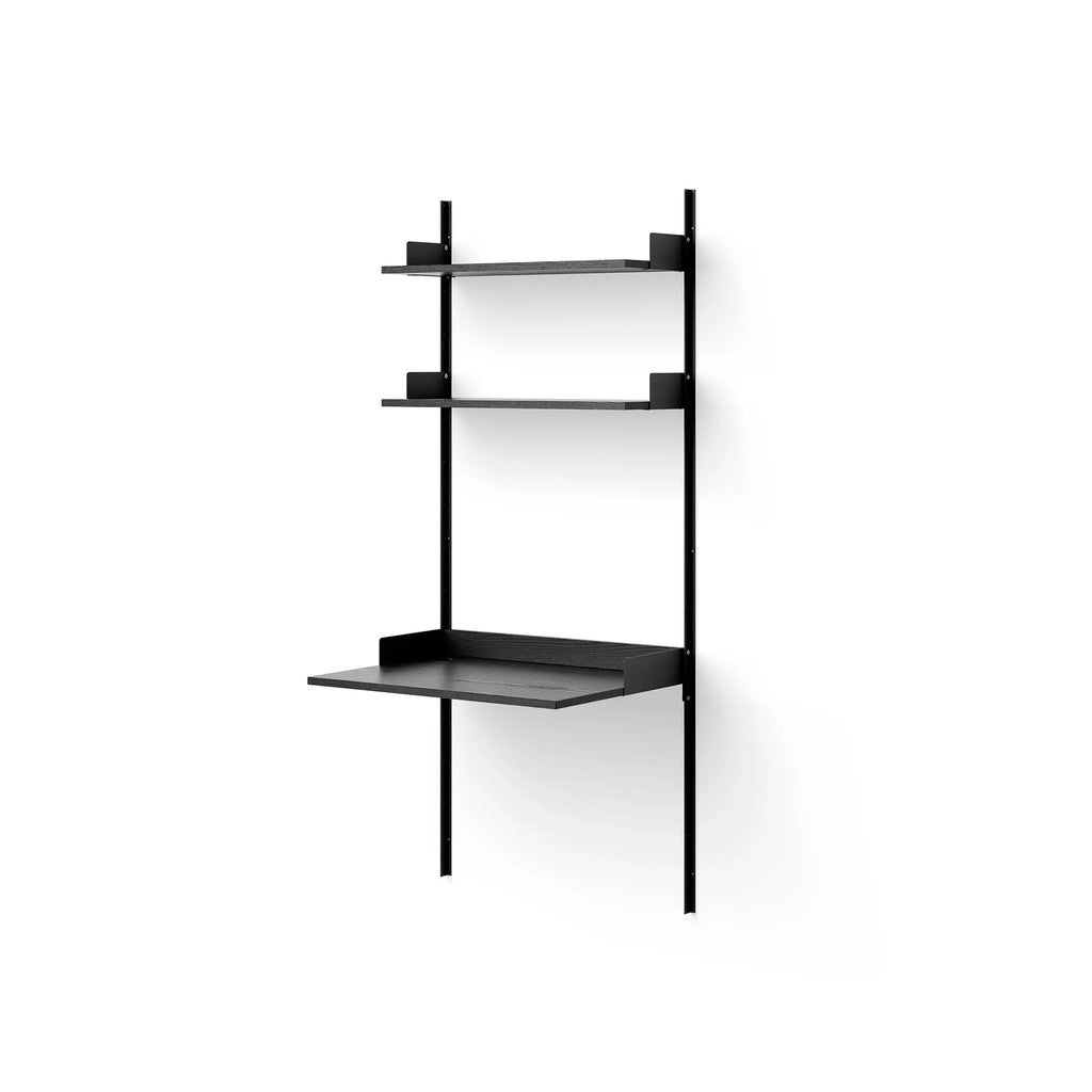 New Works Study Shelf, a modern minimalist wall-mounted shelving unit featuring matte black powder-coated metal uprights and brackets supporting three dark stained ash wood shelves, one of which functions as a floating desk. This Scandinavian-inspired black wall desk system offers sleek storage and a compact workspace for contemporary interiors. Ideal for a home office, small apartment living room, or bedroom study nook.