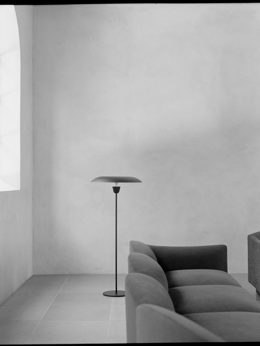 New Works Kantarell Floor Lamp, a sleek modern minimalist floor lamp featuring a slim matte black metal stem and a wide, flat, mushroom-like dark metal shade designed to cast a downward glow. This contemporary Scandinavian-inspired lighting fixture offers subtle illumination with its unique organic shape. Perfect as a designer floor lamp for a living room reading nook or an organic modern bedroom accent.