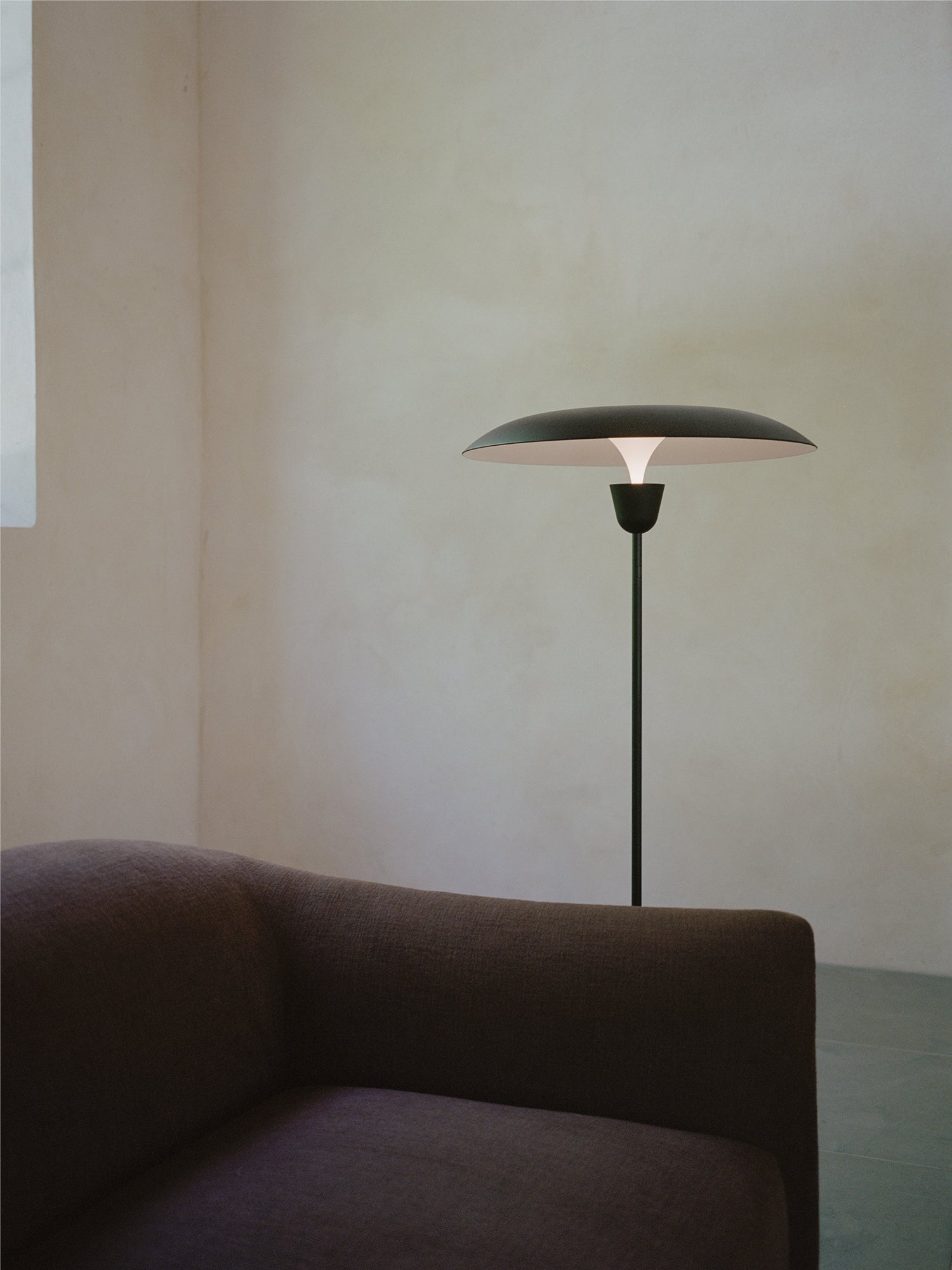 New Works Kantarell Floor Lamp, a modern minimalist floor lamp featuring a slender matte black metal stem and a wide, disc-shaped shade with a contrasting white interior, casting a warm, downward glow. Its organic mushroom-like silhouette embodies contemporary Scandinavian design. Perfect as an ambient reading lamp or a stylish accent in living rooms and bedrooms.