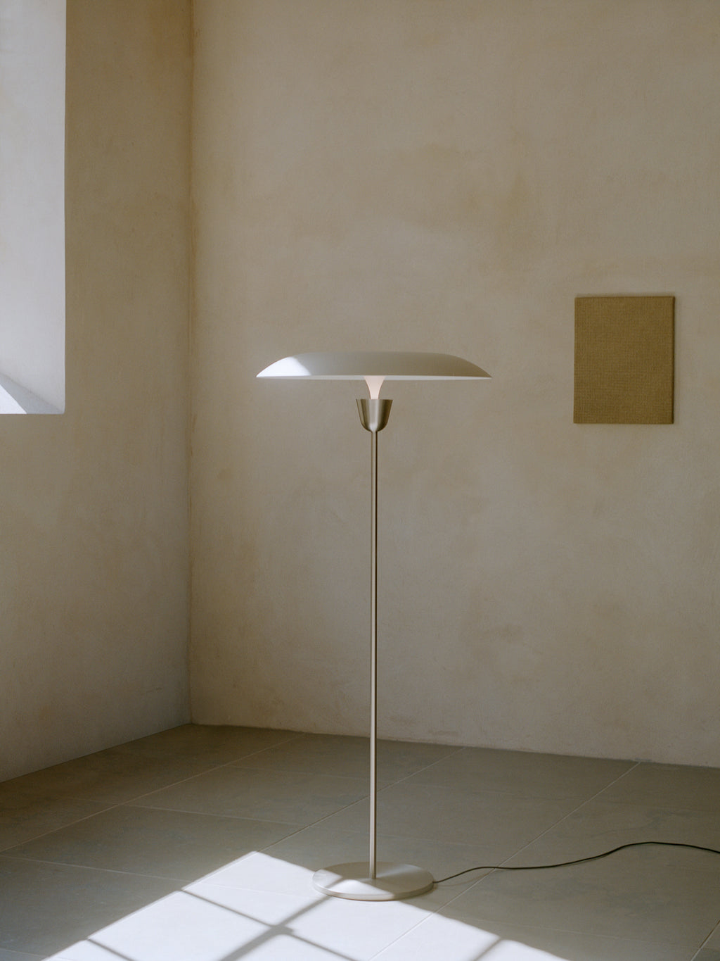 New Works Kantarell Floor Lamp, a sleek modern minimalist floor lamp featuring a slender brushed steel column and a wide, flat, matte white mushroom-shaped shade that directs a soft upward glow. This contemporary Scandinavian design, with its round base and clean lines, offers ambient lighting. Perfect as a designer standing lamp for a minimalist living room, cozy reading nook, or stylish bedroom accent.